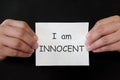 Not guilty, innocent and justice miscarriage concept. Hands holding paper placard mug shot with written word in dark black