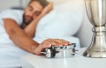 Not today alarm clock, not today. a tired young man sleeping in his bed while turning off the alarm clock. Royalty Free Stock Photo