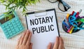 NOTARY PUBLIC is written in white on a black board next to a phone, notepad, glasses, pencils and a green plan Royalty Free Stock Photo