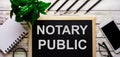 NOTARY PUBLIC is written in white on a black board next to a phone, notepad, glasses, pencils and a green plant Royalty Free Stock Photo