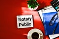 NOTARY PUBLIC is written in a white notepad near a green plant, calculator, cup coffee, glasses and a pen on a red background Royalty Free Stock Photo