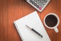 Note book with pen and a cup of coffee on wood table.