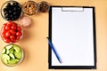 Note pad with pen and six bowls with tomatoes, black olives, fresh cucumbers, colored peppers, pink salt and walnuts Royalty Free Stock Photo
