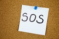 Note with SOS inscription. Sticky note with SOS inscription pinned on a cork bulletin board