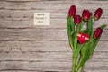 A note wishing you a happy mother`s Day and a spring bouquet of red tulips on a wooden background.