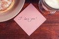 A note with the words `I love you` and a Cup of cappuccino on a wooden table