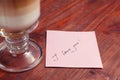 A note with the words `I love you` and a Cup of cappuccino on a wooden table