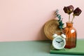 Notebook, alarm clock, vase of dry flower on green desk. pink wall background Royalty Free Stock Photo