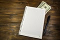 Notebook with ballpoint pen and dollar banknotes on the wooden desk Royalty Free Stock Photo