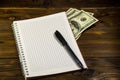 Notebook with ballpoint pen and dollar banknotes on the wooden desk Royalty Free Stock Photo