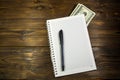 Notebook with ballpoint pen and dollar banknotes on the wooden desk Royalty Free Stock Photo