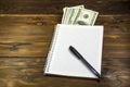 Notebook with ballpoint pen and dollar banknotes on the wooden desk Royalty Free Stock Photo