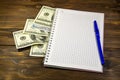 Notebook with ballpoint pen and dollar banknotes on the wooden desk Royalty Free Stock Photo