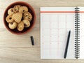 Notebook with black pen and pile of biscuit cookies in brown ceramics plate on wooden table floor Royalty Free Stock Photo