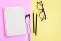 Notebook,Black pencil,Eyeglasses and Black Wired Earphones  on pink and yellow background Royalty Free Stock Photo