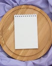 Notebook with blank cover and circular cutting Board on a purple striped tablecloth