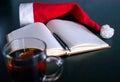 A Notebook with Blank Pages, Black Pen, Santa Hat, Glass Mug with Teabag, on the Desk. New Year`s resolution, Planning Future