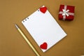 A notebook with a blank white sheet and two red hearts lies between a red gift box and a yellow pen. Concept photo Royalty Free Stock Photo