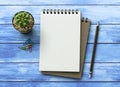 Notebook on blue wooden table with a plant, paper clip and pencil. Blank notepad paper for input copy or text. Top view desk, flat Royalty Free Stock Photo