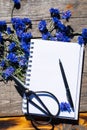 A Notebook And A Bouquet Of Cornflowers. Flowers Of Blue Wildflowers With An Empty Notepad For Notes On A Wooden Table.