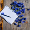 A Notebook And A Bouquet Of Cornflowers. Flowers Of Blue Wildflowers With An Empty Notepad For Notes On A Wooden Table