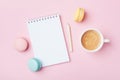 Notebook, cup of coffee and colorful macaron on pastel pink desk top view. Cozy morning breakfast. Fashion flat lay.