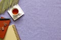 Notebook, cup of tea, clip, pen, green leaf on purple fabric background Royalty Free Stock Photo