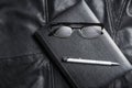 Notebook, glasses and pix over black leather background