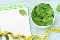 Notebook, green spinach leaves and tape measure on wooden table top view. Diet and healthy food.