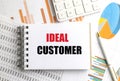 Notebook with ideal customer text on desk with charts, graphs, calculator and pen representing target audience analysis Royalty Free Stock Photo
