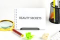 A notebook labeled beauty secrets sits in a creative workspace alongside a magnifying glass and colorful crumpled paper. The Royalty Free Stock Photo