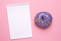 Notebook and lilac sweet donut on a pink background flat lay