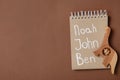 Notebook with list of baby names and wooden toy on brown background, top view. Space for text Royalty Free Stock Photo