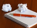 A notebook, an orange pen and two smashed paper sheet balls on dark wood background. Royalty Free Stock Photo