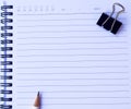 Notebook paper with white pencil and black paper clip on white background for texture Royalty Free Stock Photo