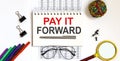 Notebook with PAY IT FORWARD word with office tools on white table Royalty Free Stock Photo