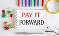 Notebook with PAY IT FORWARD word with office tools on the white table Royalty Free Stock Photo