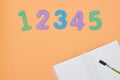 Notebook, pen and colored numbers on orange background. Accessories for study. Top view, flat, copy space. the concept of school