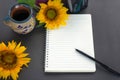 Notebook with pen, morning cup of coffee and sunflowers on the gray table background. Top view. Flat lay working table.