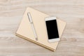 Notebook and pen placed next to a smartphone on a wooden surface during the day Royalty Free Stock Photo