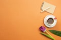 Notebook, pencil, cup of coffee, tulip flower on orange background