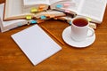 Notebook and pencil with a cup of tea in front of pile of books with bookmarks