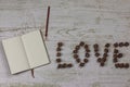 Notebook with a pencil next to the inscription I love you, the letters of dark roses. On wooden background, photo above.