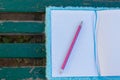 Notebook and pencil placed on the green bench on a sunny day