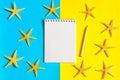 Notebook, pencil with sea stars on blue and yellow paper background. Mock up, flat lay, copy space, top view. Summer vacation Royalty Free Stock Photo