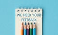 A notebook with pencils on it that says We need your feedback. Royalty Free Stock Photo