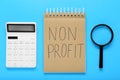 Notebook with phrase Non Profit, calculator and magnifying glass on light blue background, flat lay Royalty Free Stock Photo