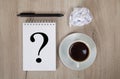 Notebook with question mark, coffee, black pen and crumpled paper. Light colored wooden background Royalty Free Stock Photo