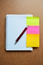 Notebook, red pen, green, pink yellow note paper on wooden background. Royalty Free Stock Photo