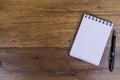 Notebook on right side of wooden table with pen aside